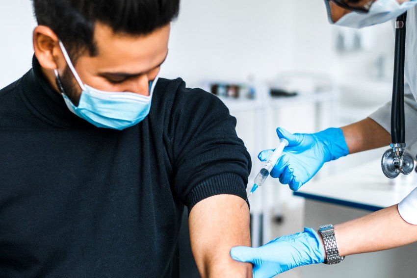 Healthcare worker administering a vaccine injection to a masked patient’s upper arm.