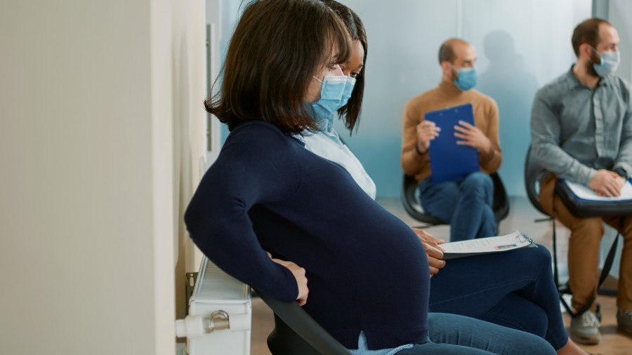 Pregnant woman wearing a face mask sits in a waiting room